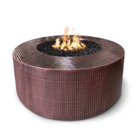Round Unity Hammered Copper fire pit table with glowing flames, outdoor patio setting