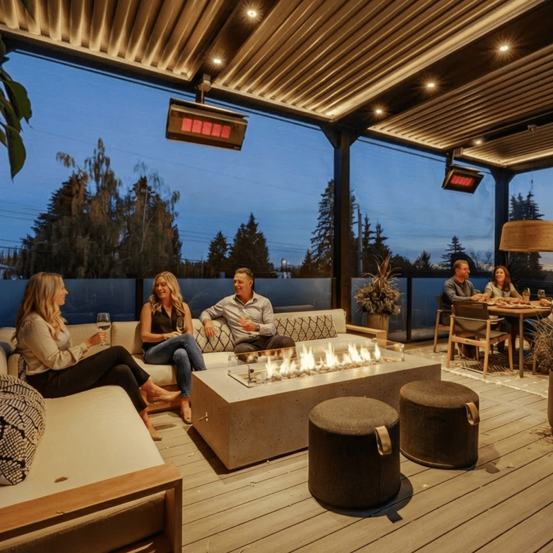 Bromic Platinum Gas heaters suspended above a covered outdoor lounge and dining space at dusk. Manufacturer installation inspiration; accessories shown sold separately.