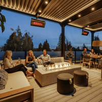 Bromic Platinum Gas heaters suspended above a covered outdoor lounge and dining space at dusk. Manufacturer installation inspiration; accessories shown sold separately.